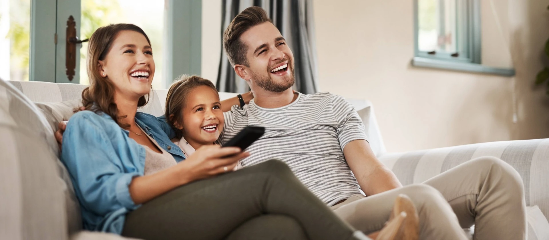 happy young family relaxing on the sofa and watching tv together at home